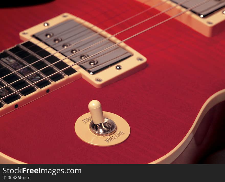 The detail of a red electric guitar showing strings, pickup and rhythm/treble switch. The detail of a red electric guitar showing strings, pickup and rhythm/treble switch