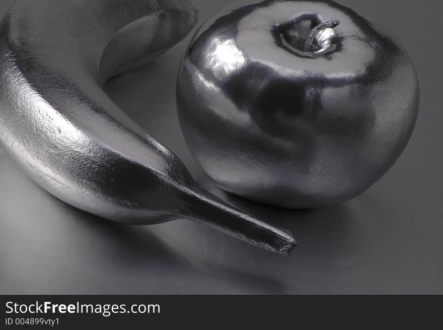 A metallic-looking banana and apple on a silver surface.