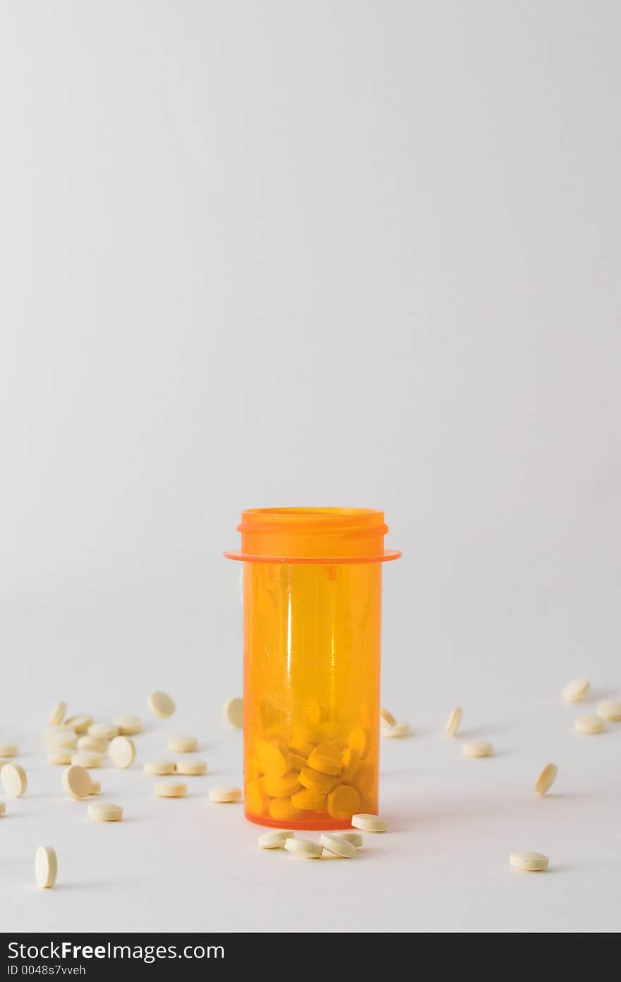 Medicine bottle on table with tablets around it; bottle is placed in the center of the frame with some pills in the bottle and some laying around it. Medicine bottle on table with tablets around it; bottle is placed in the center of the frame with some pills in the bottle and some laying around it