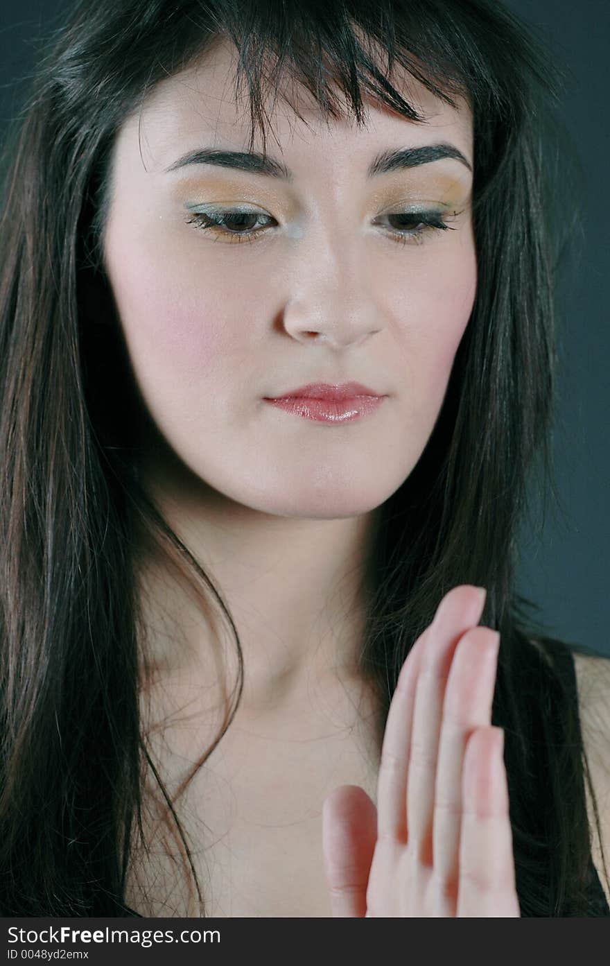 Portrait of a beautiful brunette meditates with her left hand raised in foreground, with an expression of equilibrium. Portrait of a beautiful brunette meditates with her left hand raised in foreground, with an expression of equilibrium