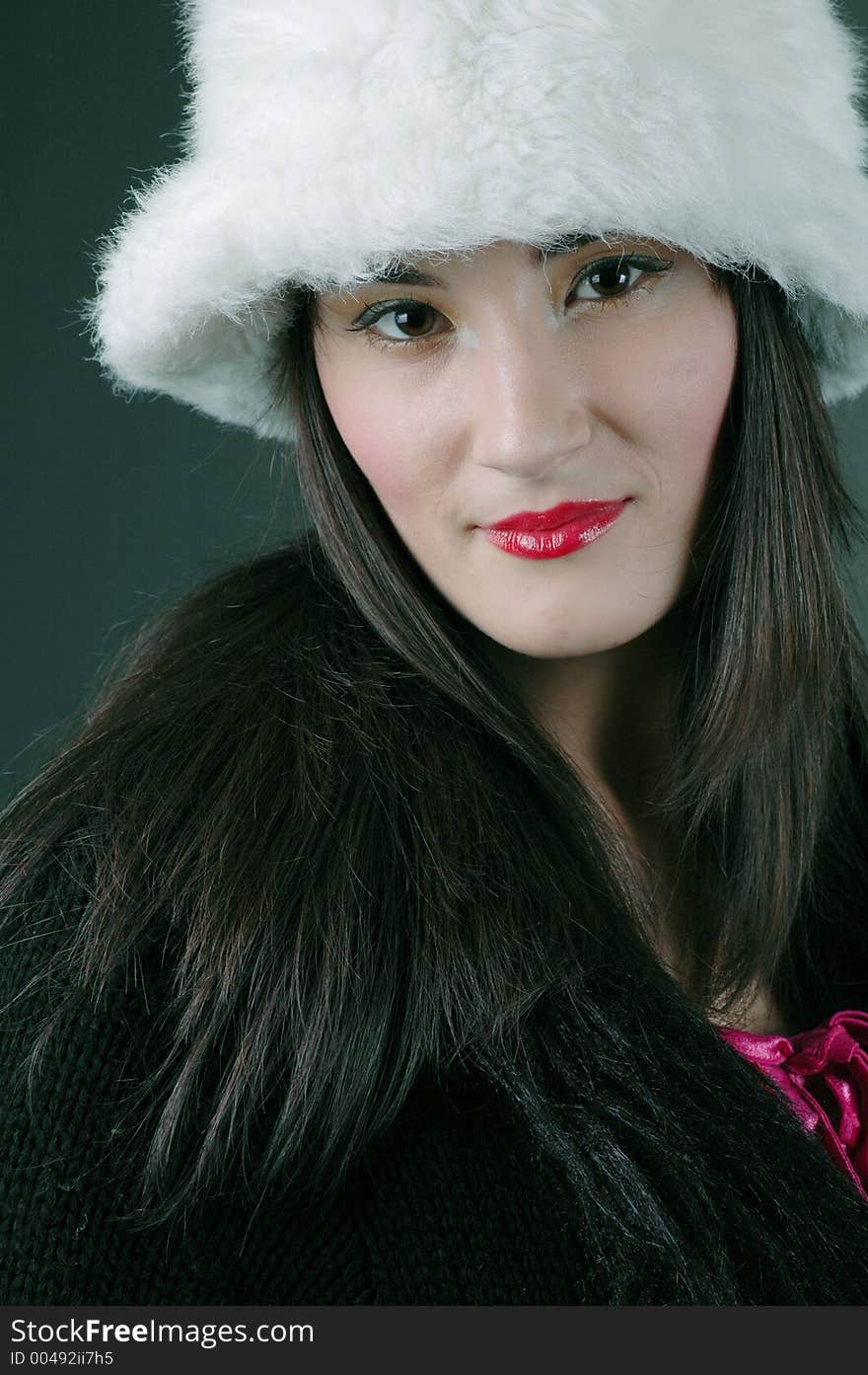 Beautiful brunette with asian features poses confidently with a white fur hat and an expression of arrogance. Beautiful brunette with asian features poses confidently with a white fur hat and an expression of arrogance