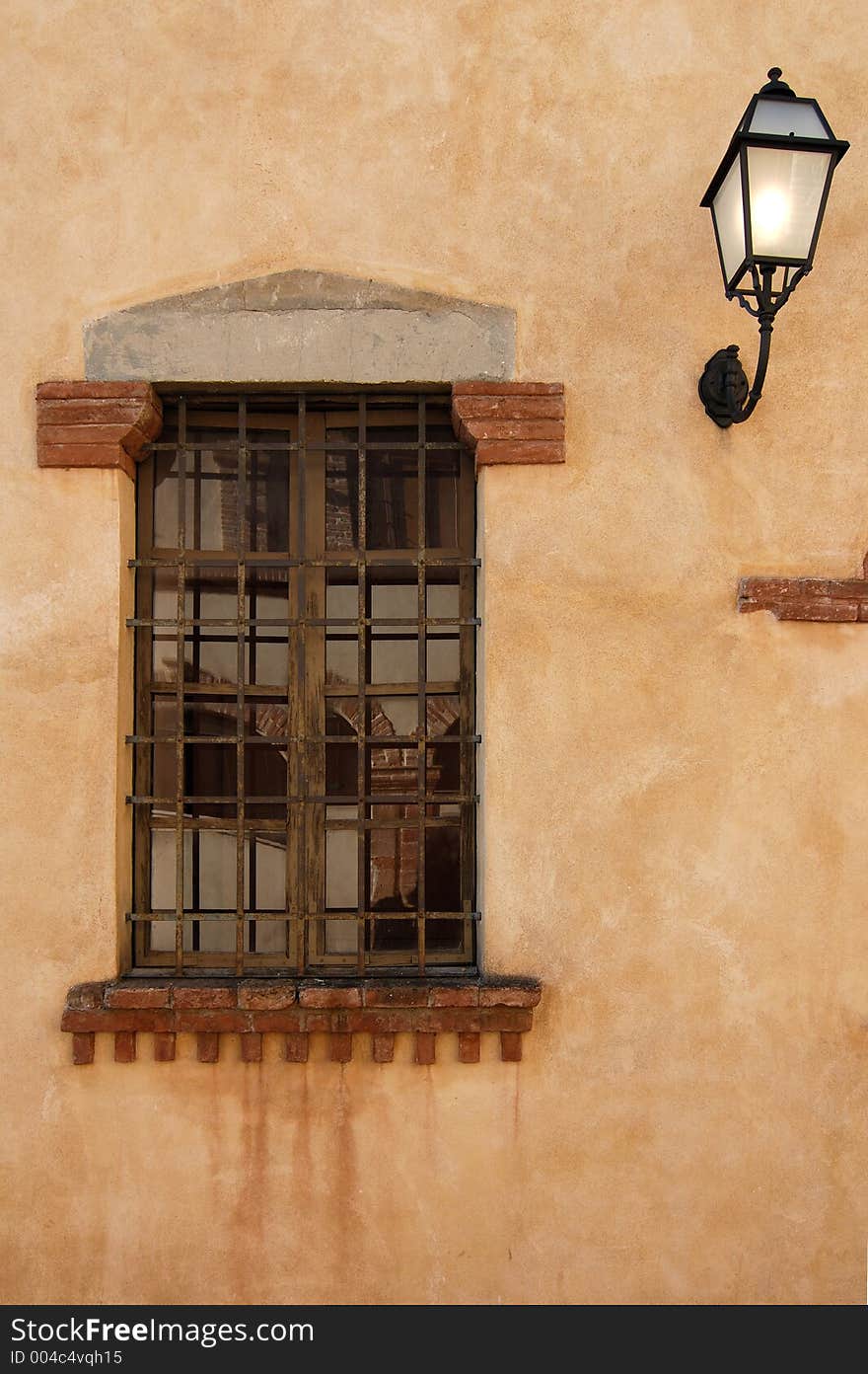 Old window protected by a grid with a lamp on the right. Old window protected by a grid with a lamp on the right