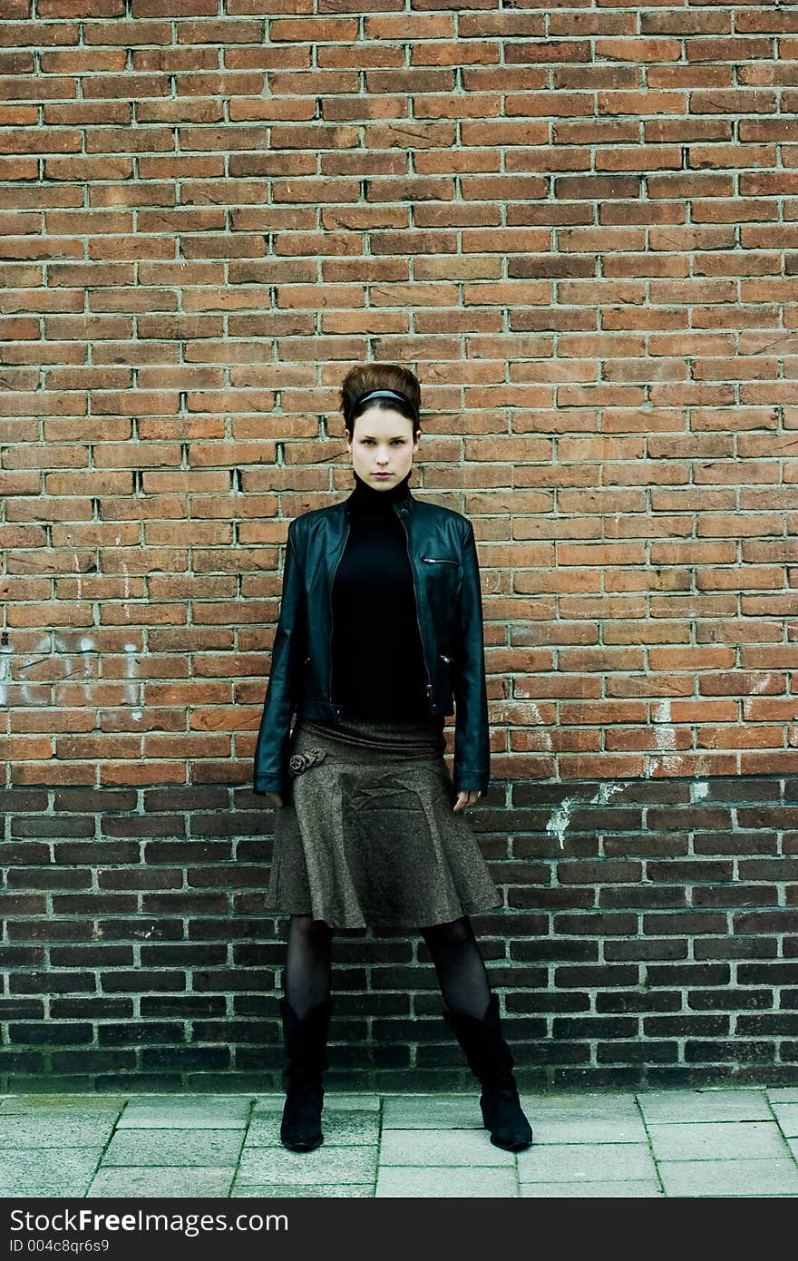 Fashionable model in skirt and leather jacket posing in front of a brick wall. Fashionable model in skirt and leather jacket posing in front of a brick wall