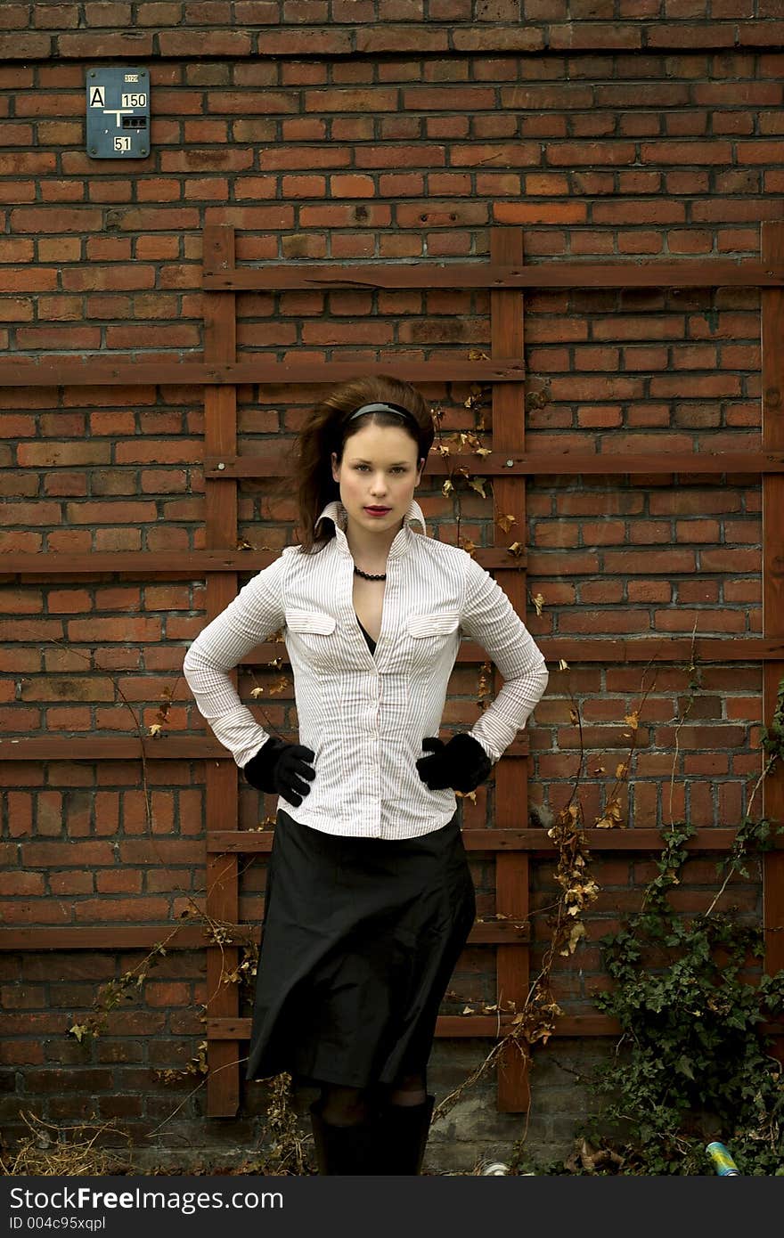 Beautiful young lady with striking green eyes in white shirt posing in front of a brick wall. Beautiful young lady with striking green eyes in white shirt posing in front of a brick wall