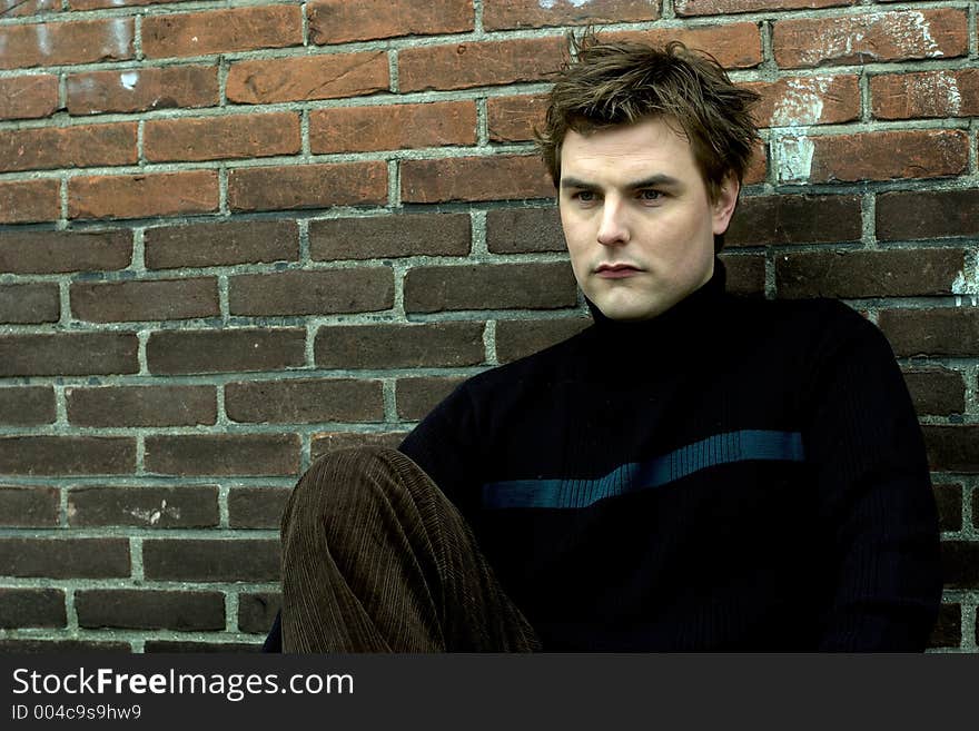 Good looking young model sitting in front of brick wall background. Good looking young model sitting in front of brick wall background