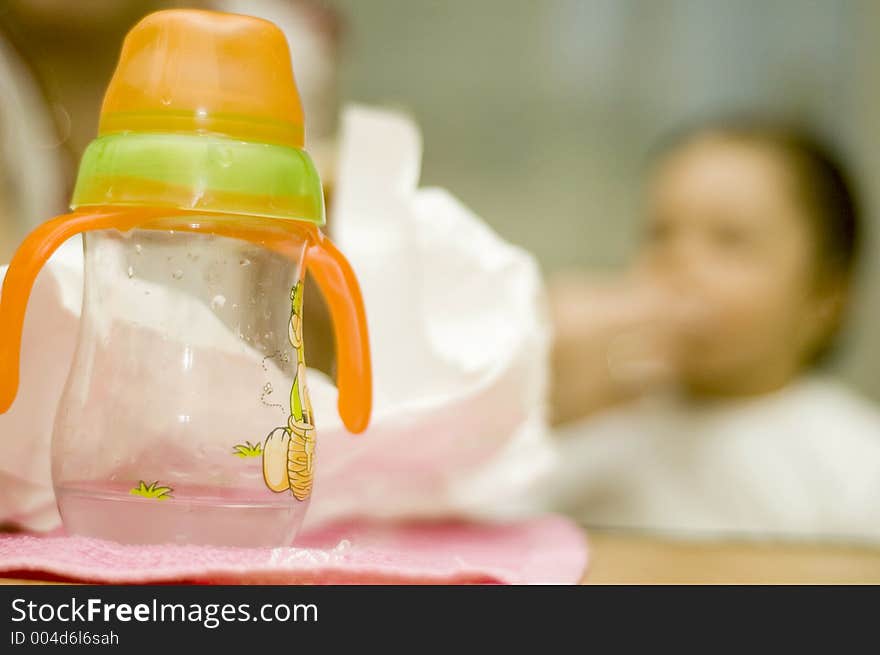 Baby bottle with wather and out of focus baby in background. Baby bottle with wather and out of focus baby in background