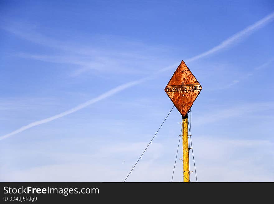 A diamond shaped rusted telephone cable sign post against a blue sky. A diamond shaped rusted telephone cable sign post against a blue sky.