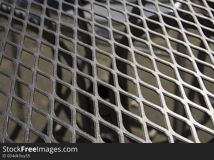 A close up of a metal grid garden table top, looking through to table base. A close up of a metal grid garden table top, looking through to table base.