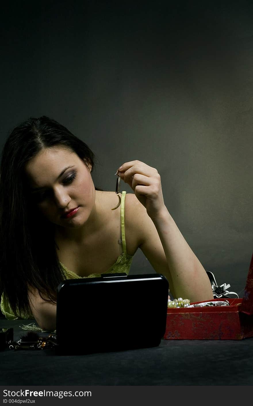 Young woman getting ready for a fancy party, putting on her earrings, looking in a compact mirror. Young woman getting ready for a fancy party, putting on her earrings, looking in a compact mirror.