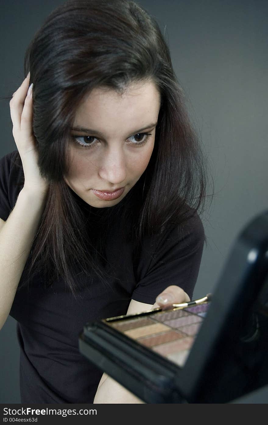 Attractive young woman holding some make-up and checking up her hair in the mirror. Attractive young woman holding some make-up and checking up her hair in the mirror