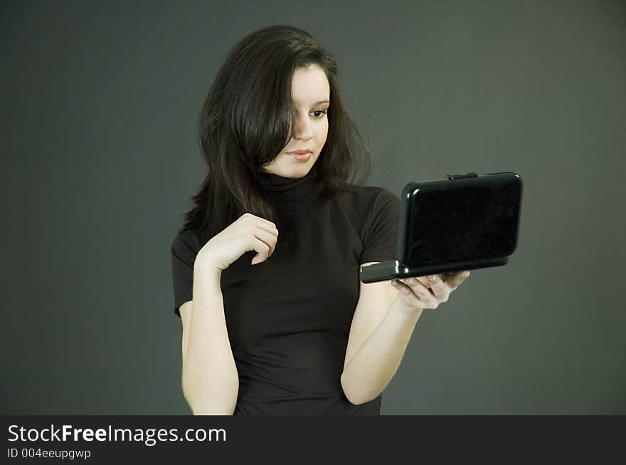 Attractive young woman holding some make-up and checking up her aspect in the mirror. Attractive young woman holding some make-up and checking up her aspect in the mirror