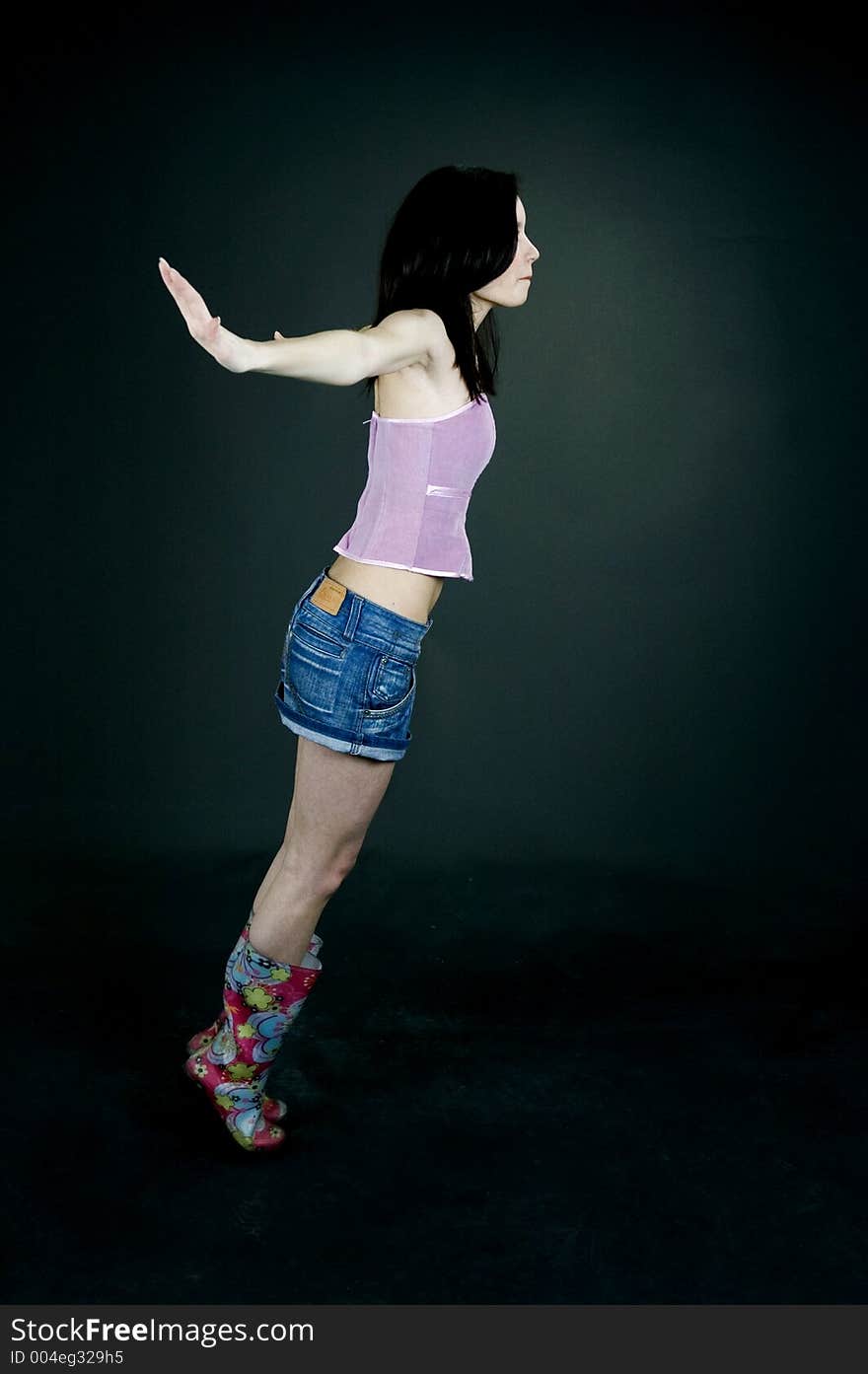 Young pretty brunette poses in the studio, dressed casual, with a light lilac top, denim skirt and colorful, funny plastic boots, trying various expressions, over a black background. Young pretty brunette poses in the studio, dressed casual, with a light lilac top, denim skirt and colorful, funny plastic boots, trying various expressions, over a black background