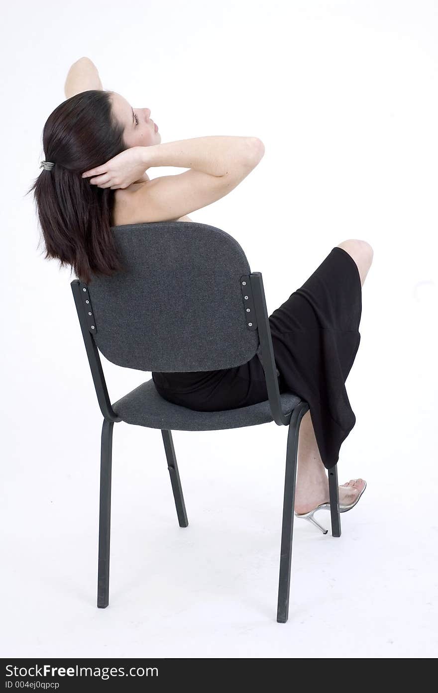 Young girl relaxes on a chair in the studio, massaging her head, shot from behind. Young girl relaxes on a chair in the studio, massaging her head, shot from behind