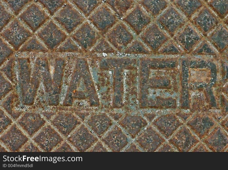 Iron cover over water turn-off valve has the word water inscribed upon it, along with decorative squares. Iron cover over water turn-off valve has the word water inscribed upon it, along with decorative squares