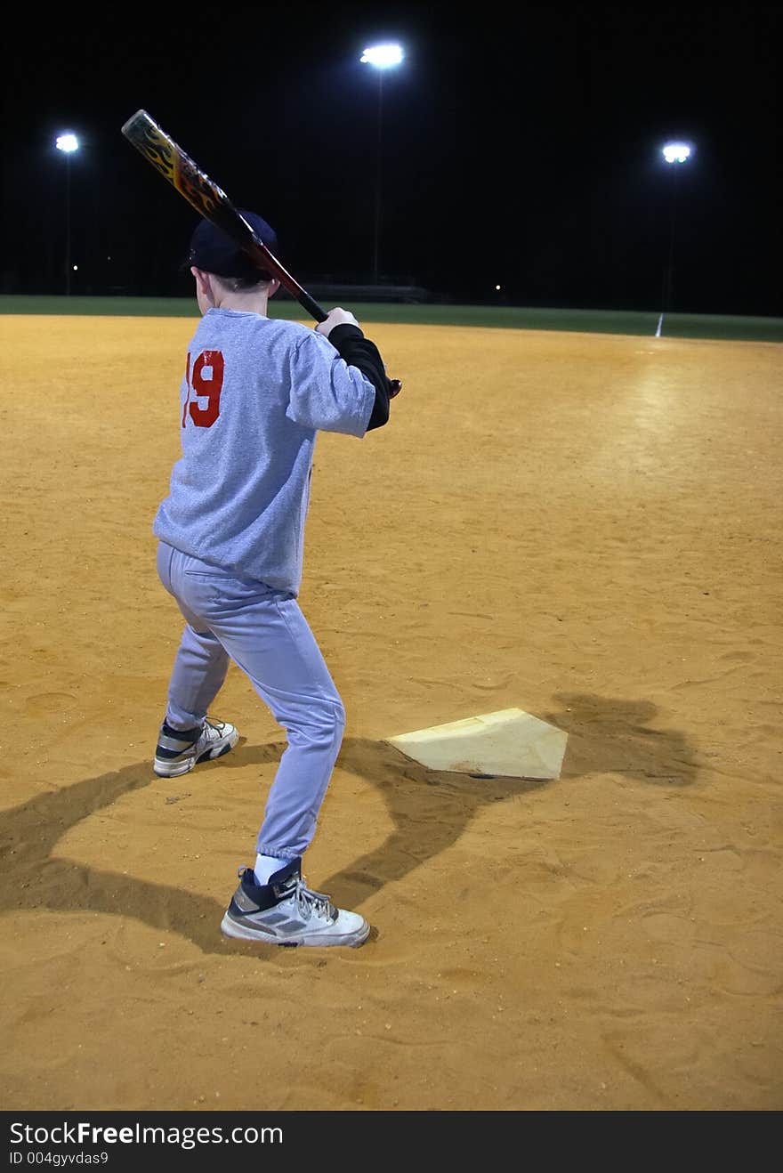 Young boy waiting for a Baseball pitch. It is night. There are stadium lights in the distance. Young boy waiting for a Baseball pitch. It is night. There are stadium lights in the distance.