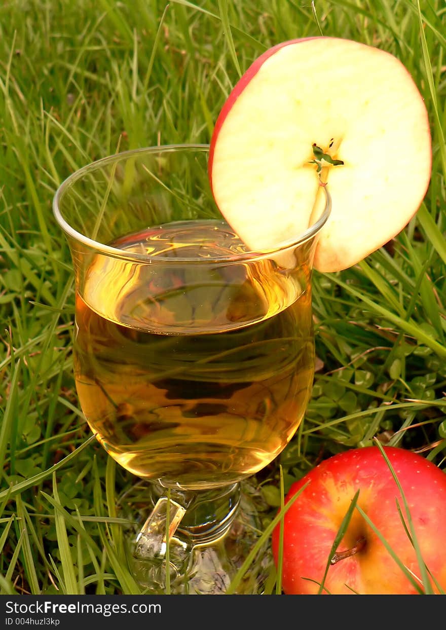 Drink in glass in the grass with an apple slice. Drink in glass in the grass with an apple slice