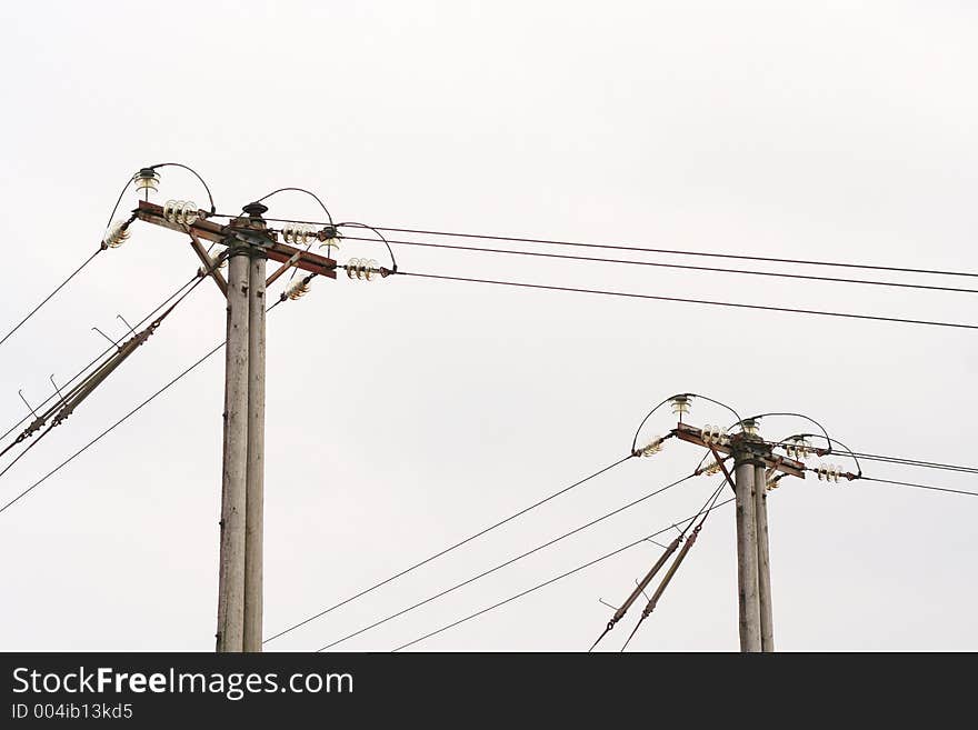 Two poles carrying power lines with an overcast sky behind them. Two poles carrying power lines with an overcast sky behind them.