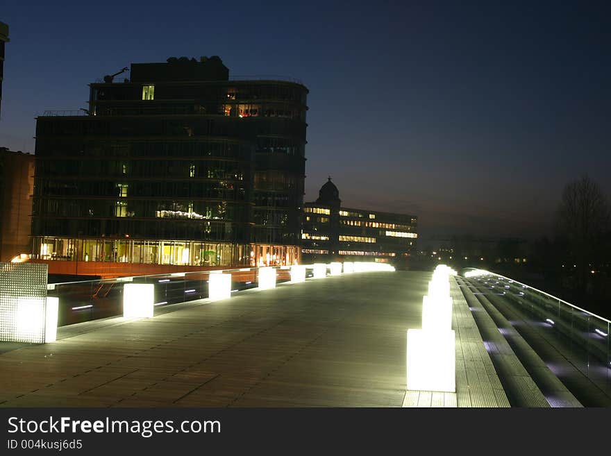 Modern pedestrian bridge in a city business district illuminated at the late evening