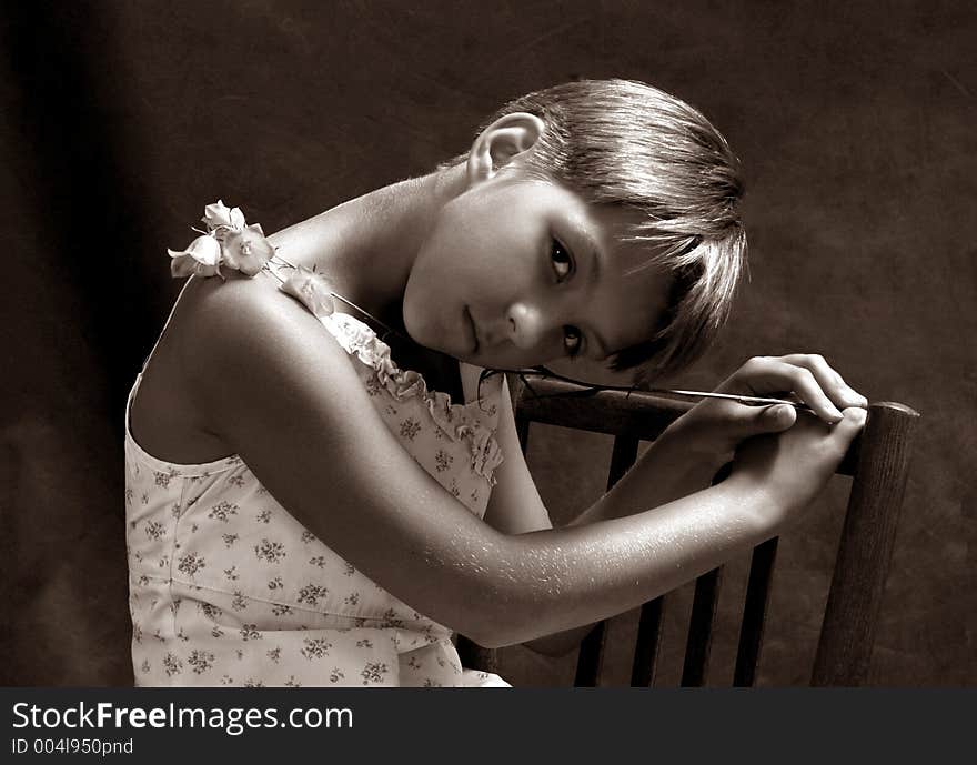 The girl sitting on a chair with a camomile on a dark background. Black-and-white. The girl sitting on a chair with a camomile on a dark background. Black-and-white.