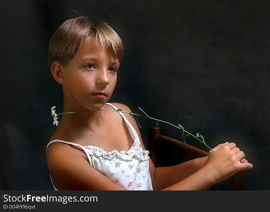 The girl sitting on a chair with a camomile on a dark background. The girl sitting on a chair with a camomile on a dark background.