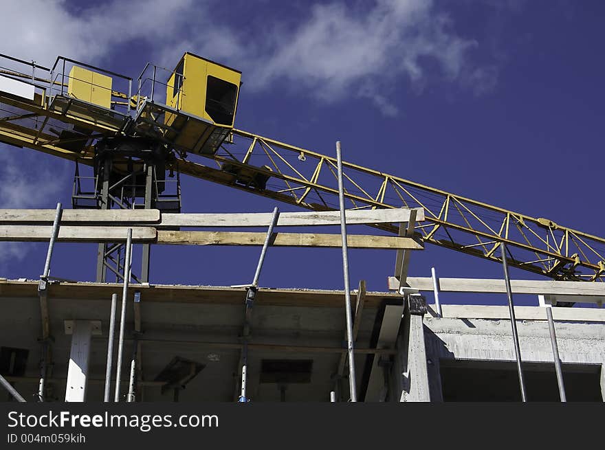 A construction place with yellow crane and scaffolding on a contrasting blue sky. A construction place with yellow crane and scaffolding on a contrasting blue sky