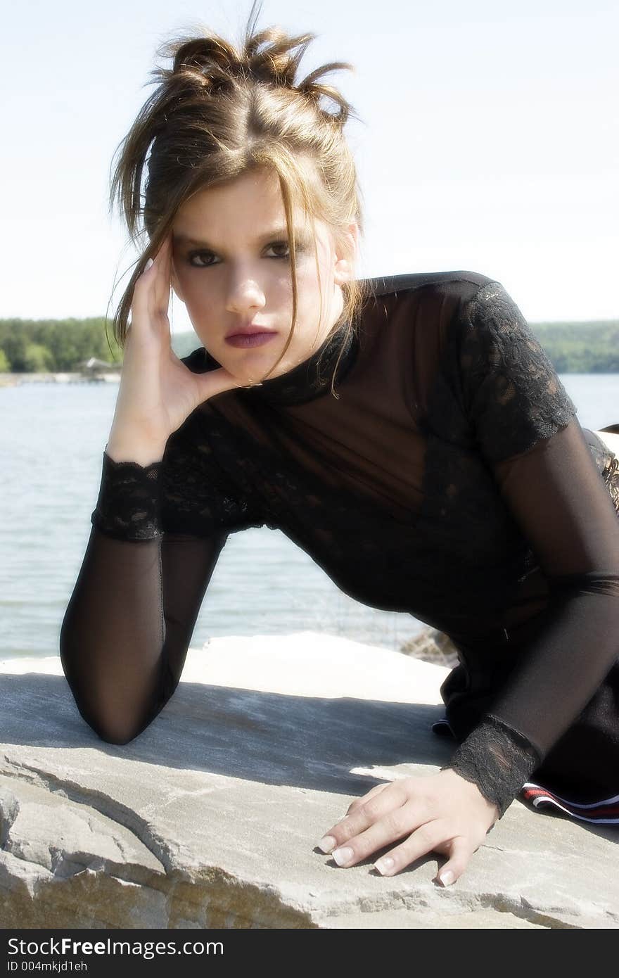 Beautiful teen girl sitting on large rock by the lake.