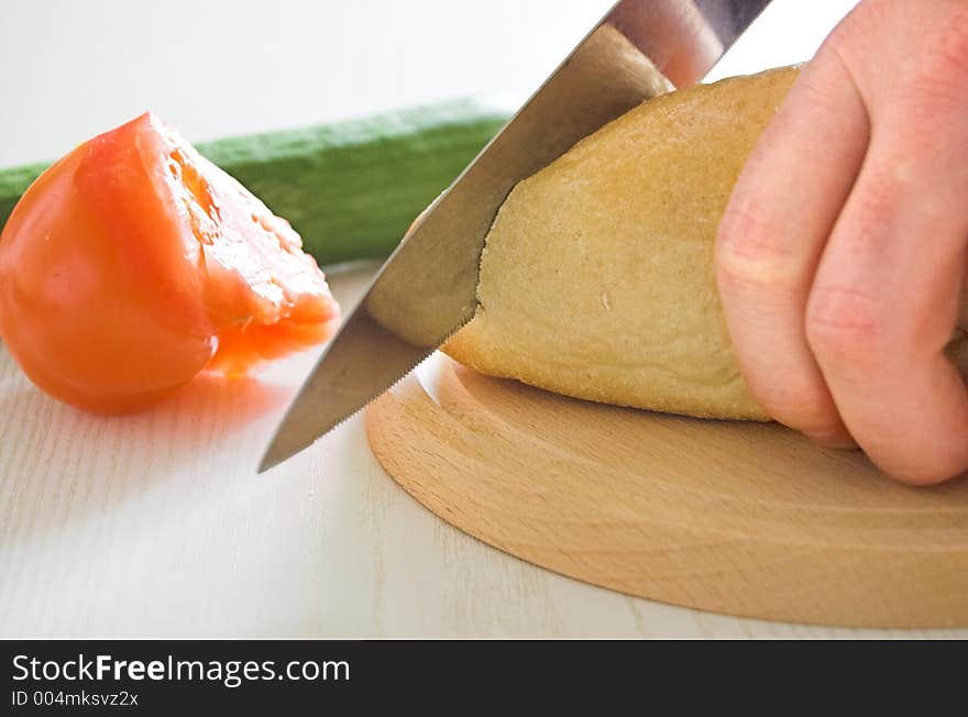 Vegetables and bread on the table in kitchen, slicing bread. Vegetables and bread on the table in kitchen, slicing bread