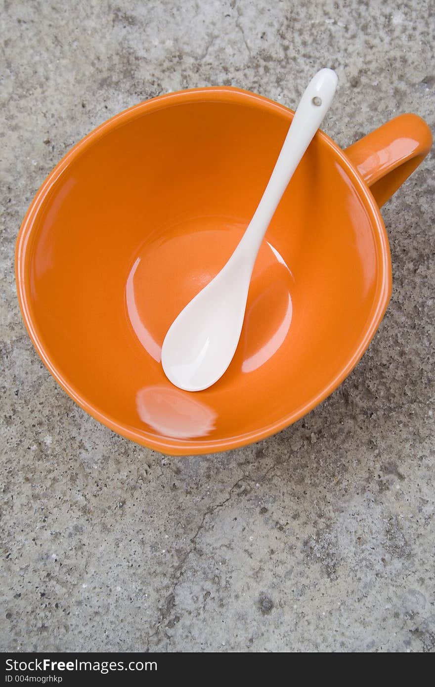 Orange cup with white spoon on a concrete table. Orange cup with white spoon on a concrete table