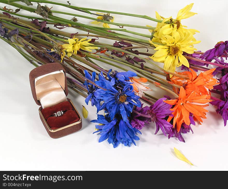 An engagement ring sets next to a tattered bouquet of flowers. An engagement ring sets next to a tattered bouquet of flowers.