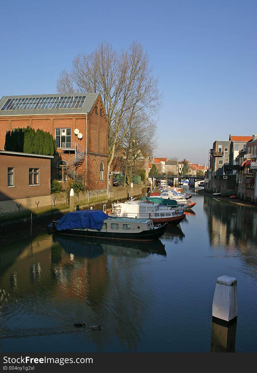 Row of boats with cabins sitting in a quiet canal surrounded by buildings. Row of boats with cabins sitting in a quiet canal surrounded by buildings