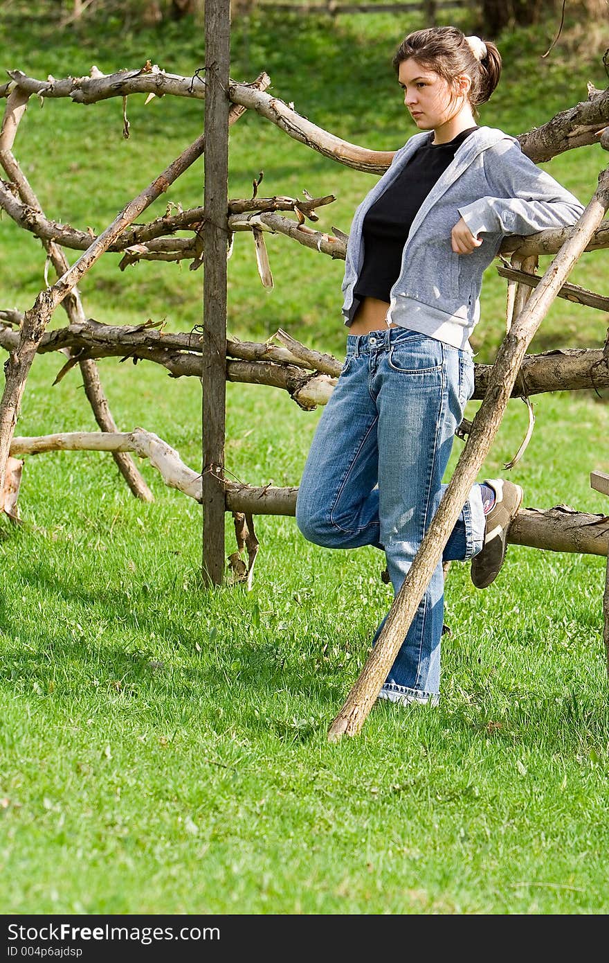 Young woman relaxing on a green field near a wooden fence. Young woman relaxing on a green field near a wooden fence