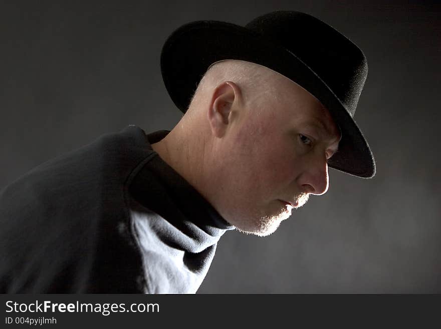 Middle aged man in profile, dark background and dark clothing and hat. Middle aged man in profile, dark background and dark clothing and hat