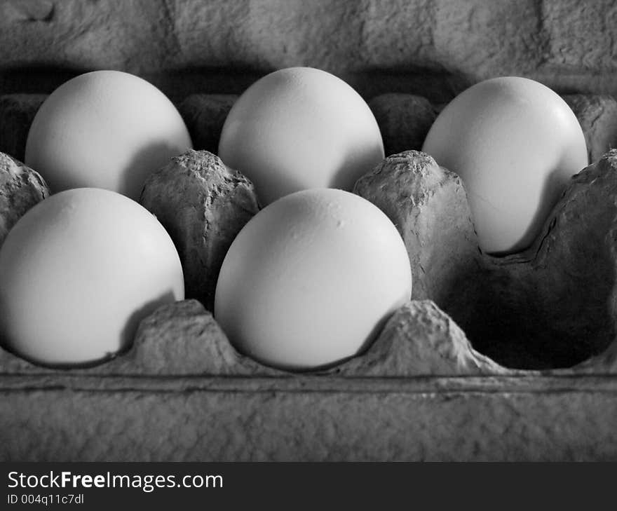 Five eggs in soft, dim light in a grey carton, arranged as to imply that an egg at the corner has been removed. Grescale image.