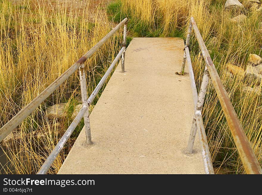 Concrete sidewalk with steel railing leading into grass and badlands.