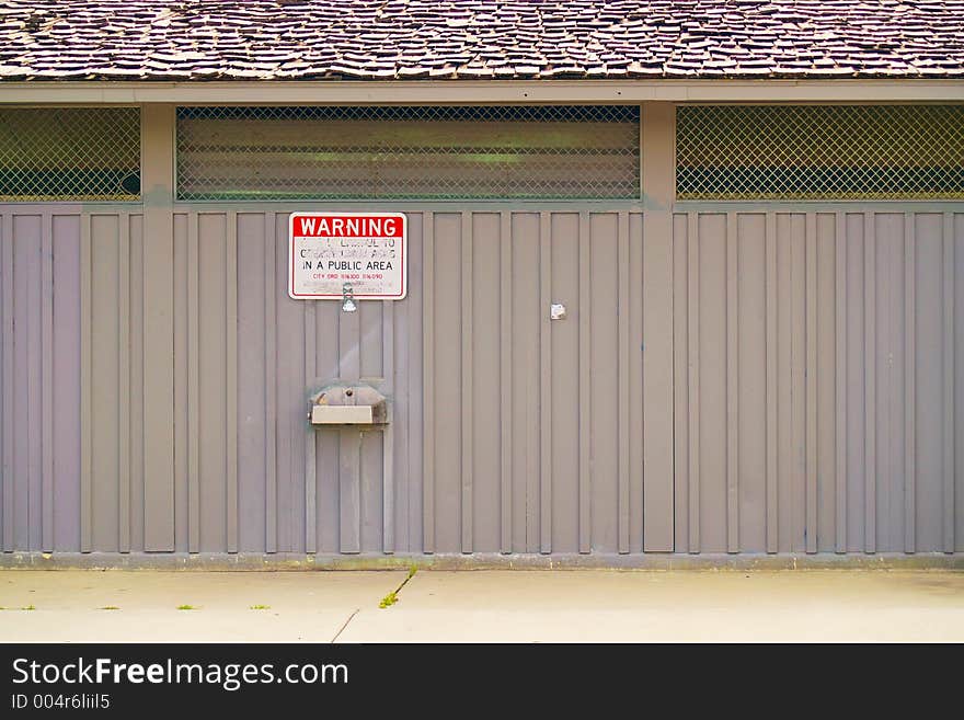 Water fountain on the side of a prefabricated steel building under a defaced or vandalized sign in a public urban area. Water fountain on the side of a prefabricated steel building under a defaced or vandalized sign in a public urban area.