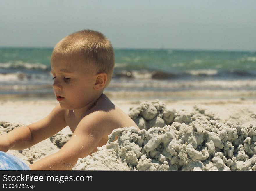 Toddler (boy) playing in the sand at the beach, build a sand castle. Toddler (boy) playing in the sand at the beach, build a sand castle