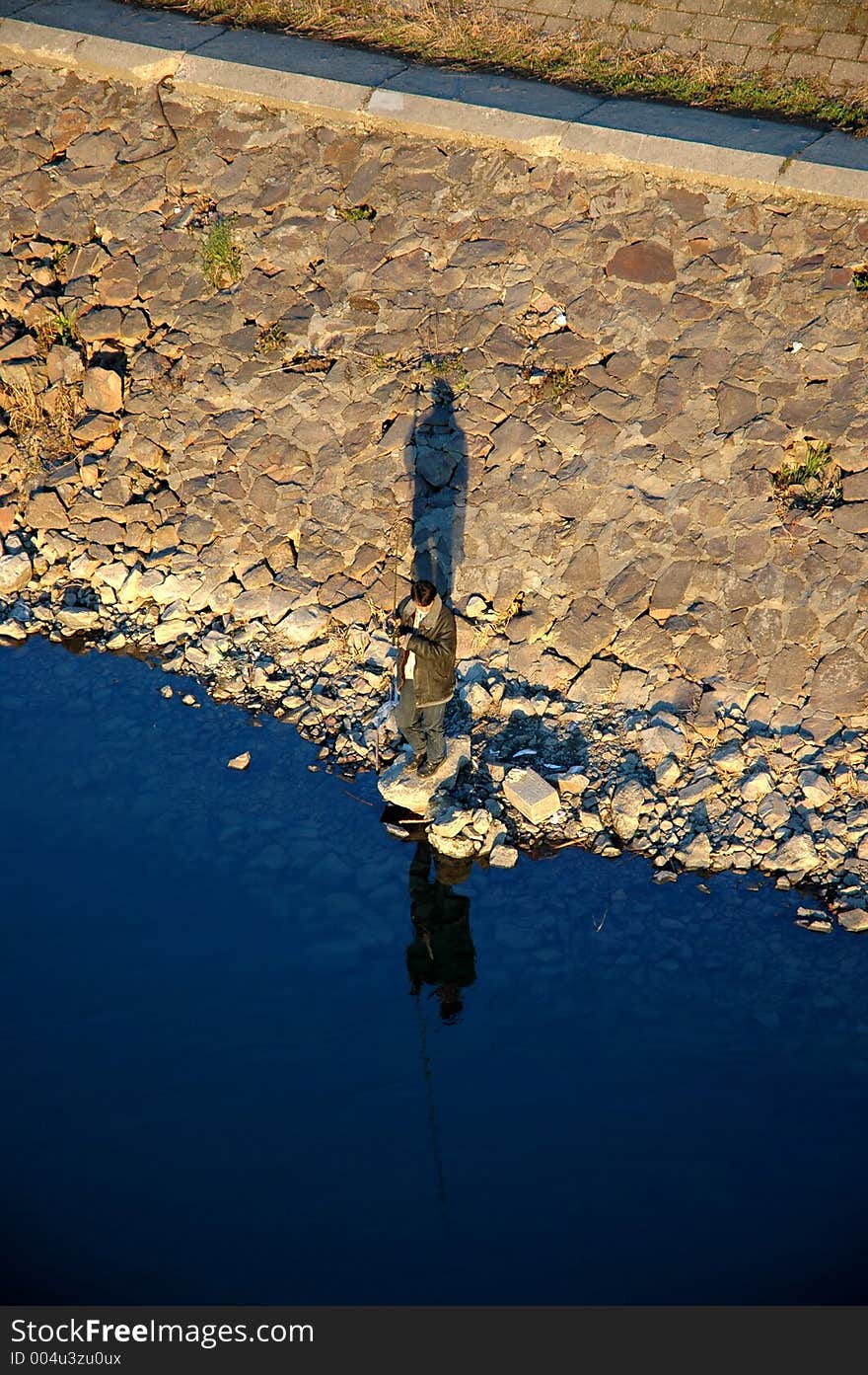 A man fishing on a bank of a river. A man fishing on a bank of a river