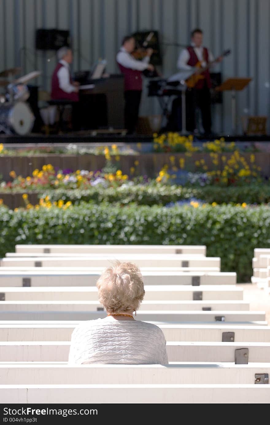 A lone elderly woman watching a jazz band in the Kurpark, Bad Homburg - Germany. Selective focus on lady. A lone elderly woman watching a jazz band in the Kurpark, Bad Homburg - Germany. Selective focus on lady.