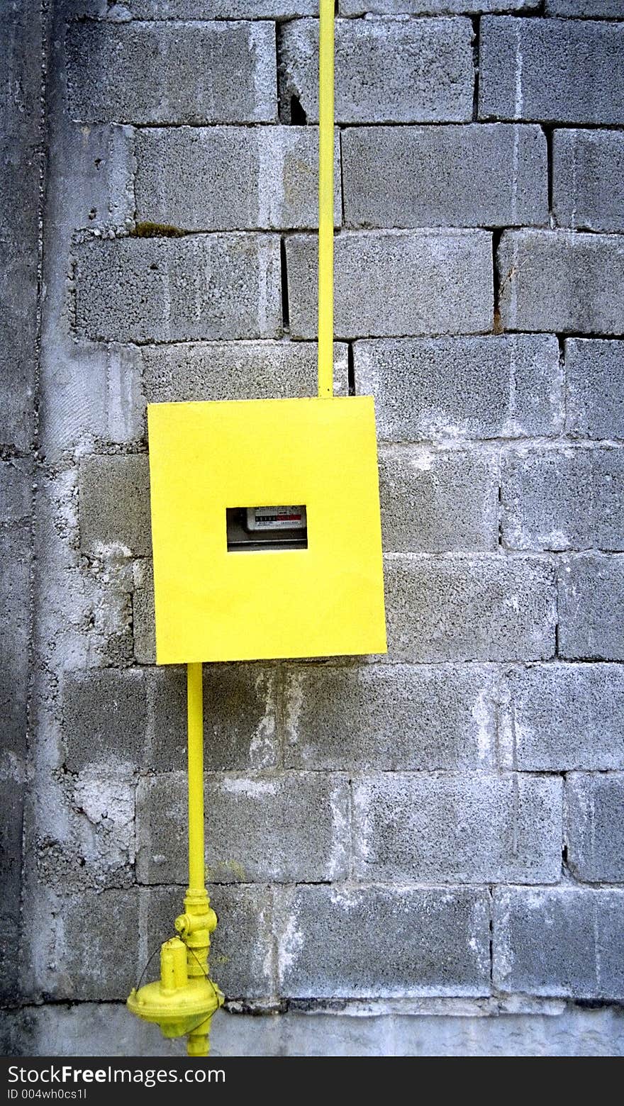 Yellow gas counter contrasting with the cement bricks wall on which it is installed. 35mm film scan