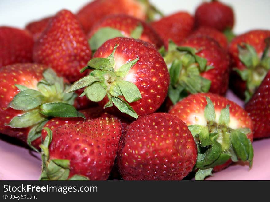 Many strawberries sit on the pink plate. Many strawberries sit on the pink plate