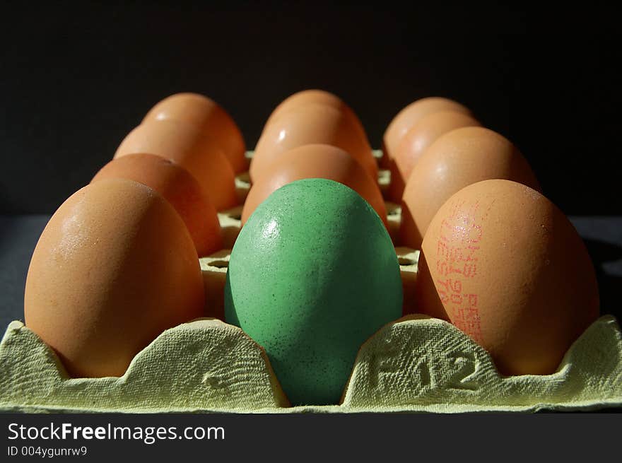 Green egg amongst normal eggs on black background. Green egg amongst normal eggs on black background