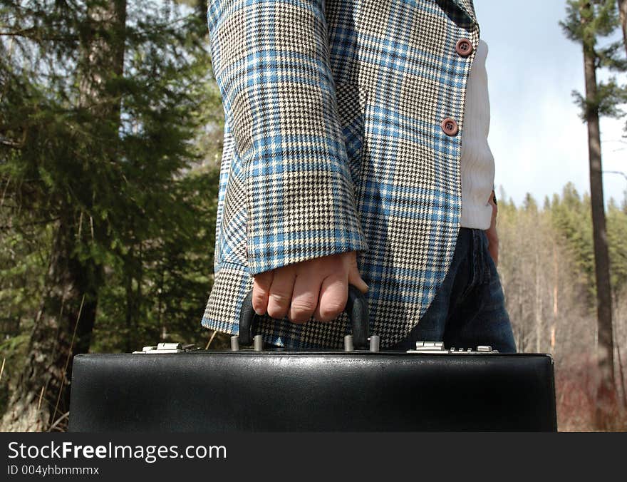 Businessman holding a briefcase outdoors in forest area.