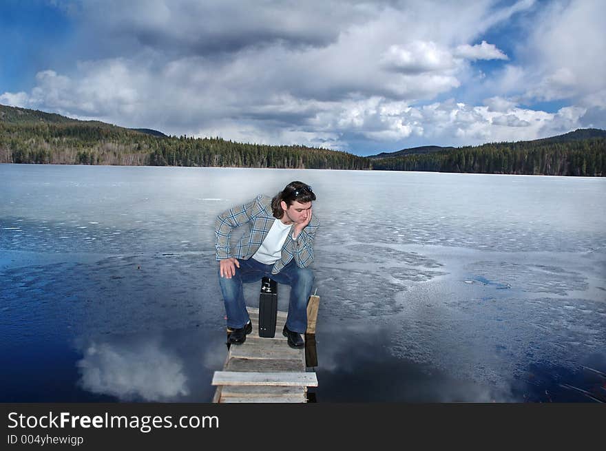 Sad looking businessman sitting on his briefcase and thinking, outdoors on a frozen lake.