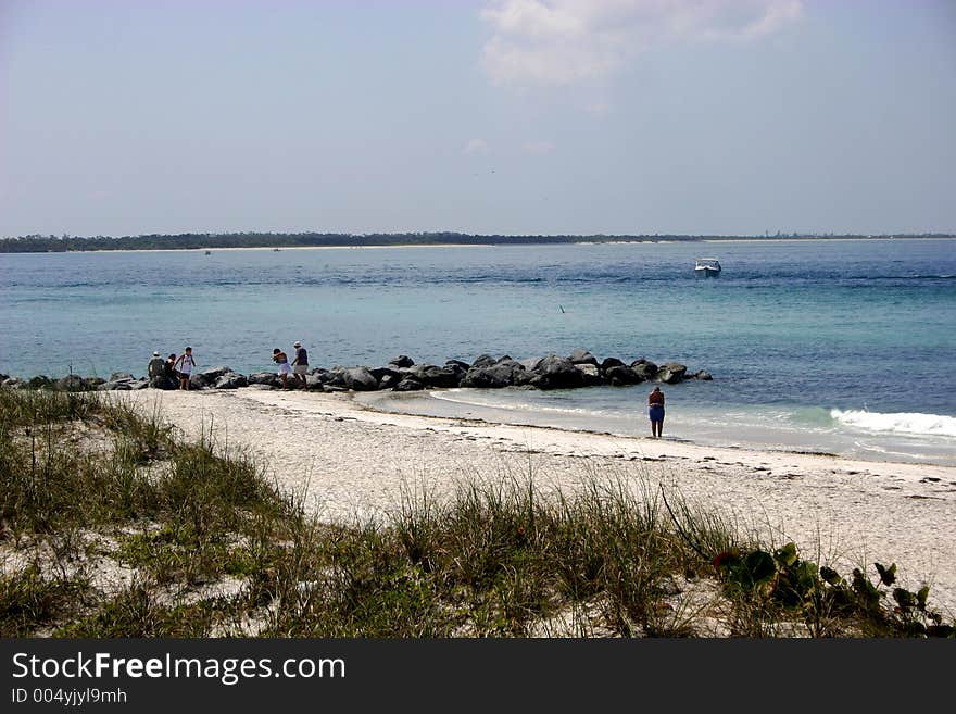 Several families enjoying the beach, showing sand dunes, rocks, waves and fishing boat out in gulf