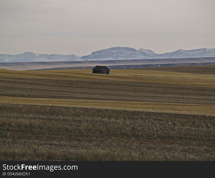 This picture was taken near Choteau, MT during a back country road drive and depicts an abandoned building in a large cultivated area with mountains in the background. This picture was taken near Choteau, MT during a back country road drive and depicts an abandoned building in a large cultivated area with mountains in the background.