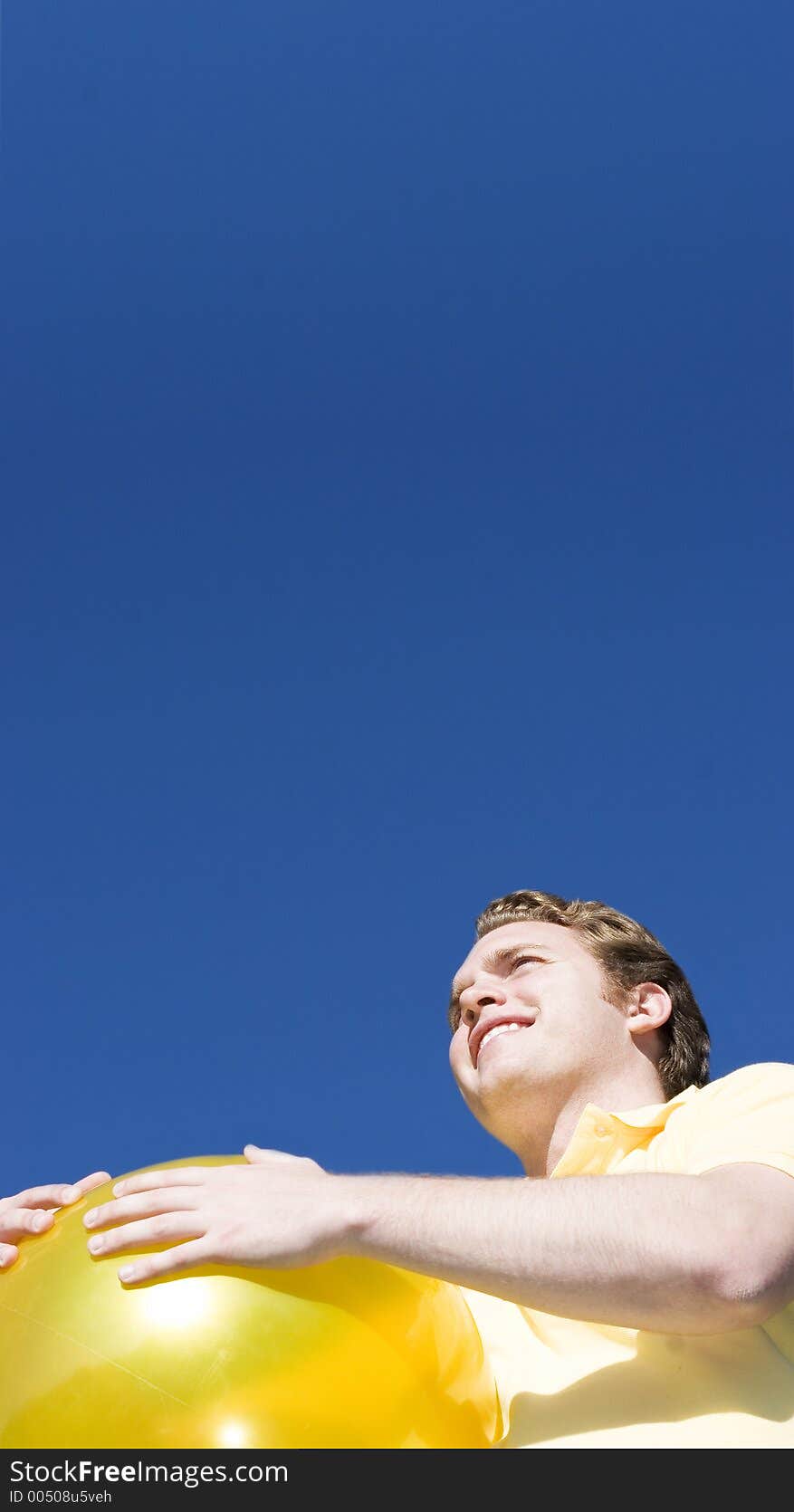 Happy Man holds a big, yellow ball and looks off to the distance under a blue sky