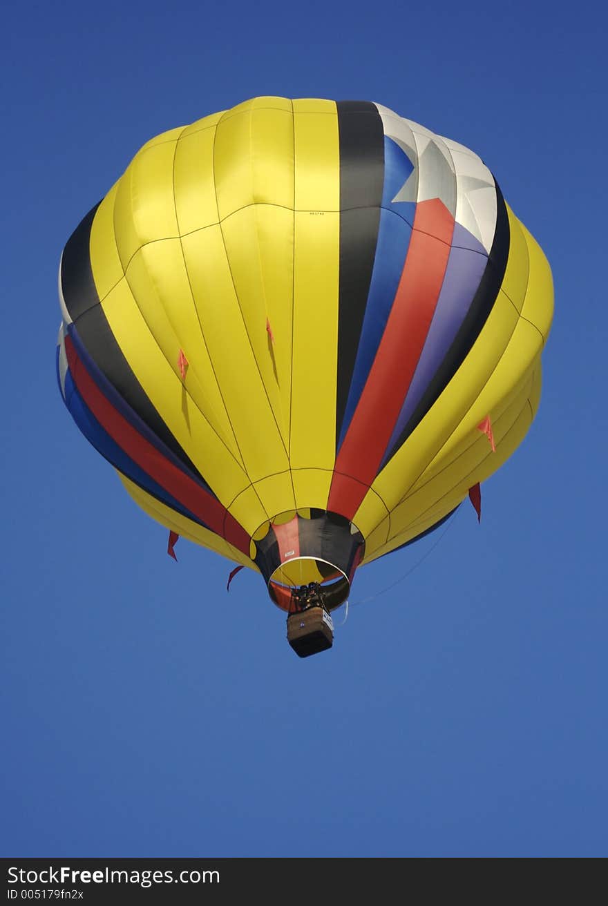 A bright yellow striped hot air balloon drifts overhead on a perfect sunny spring day.