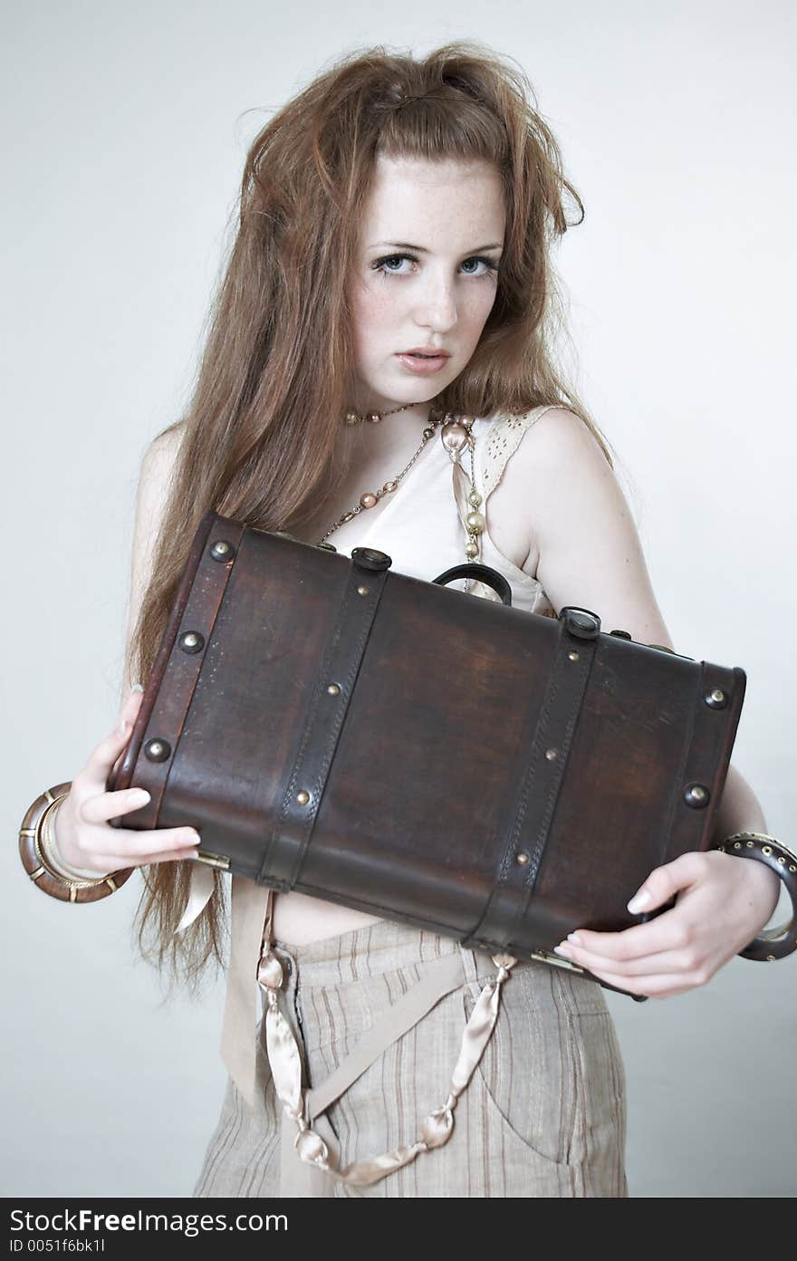 A girl with red hair. She holds a wooden suitcase in hands. The photo is executed in beige and warm tones. Studio. A girl with red hair. She holds a wooden suitcase in hands. The photo is executed in beige and warm tones. Studio