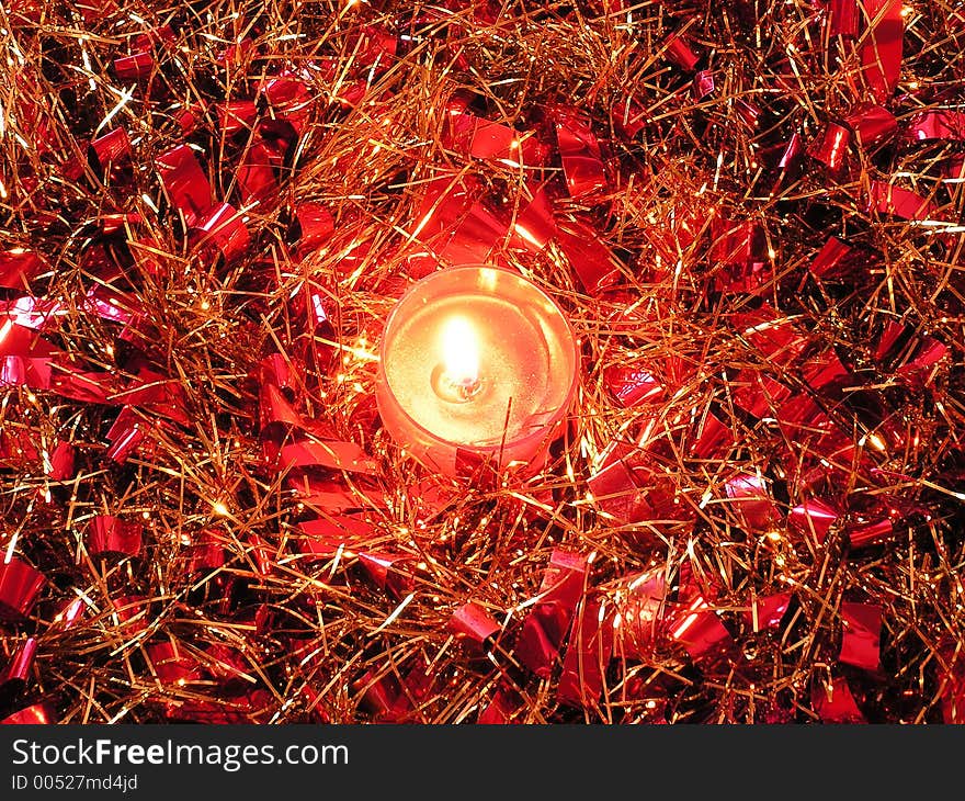 A scented candle in the centre of some swirled up red and gold tinsel. A scented candle in the centre of some swirled up red and gold tinsel.