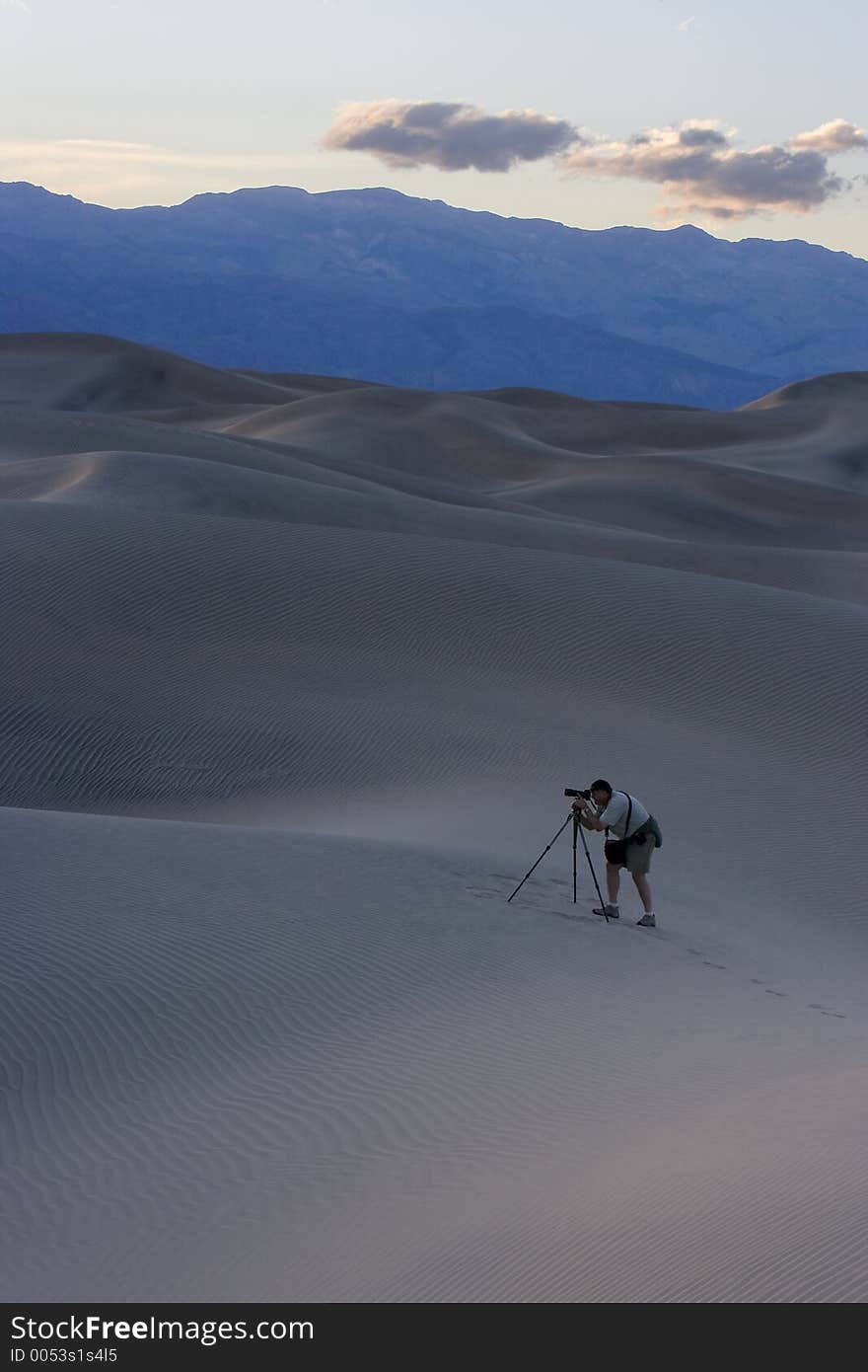 Photographer photographing the Death Valley Dunes. Early evening sky sits over softly lit sand dunes. A photograph prepares his shot in the foreground.  Death Valley, California, USA. Photographer photographing the Death Valley Dunes. Early evening sky sits over softly lit sand dunes. A photograph prepares his shot in the foreground.  Death Valley, California, USA.